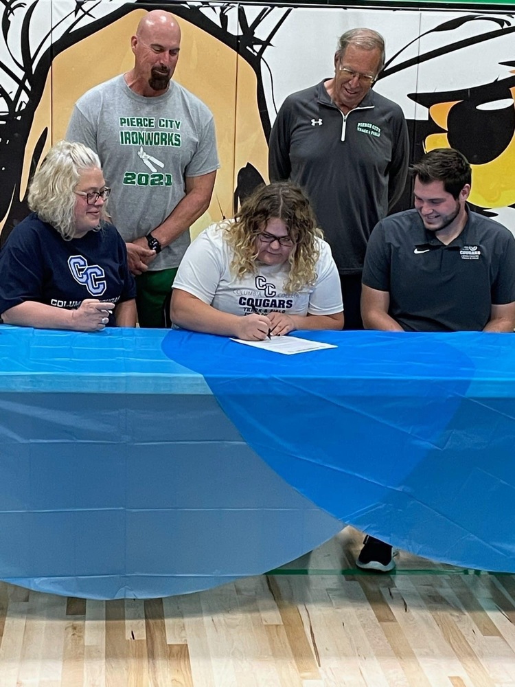 Hayden signing at table with coaches around her.